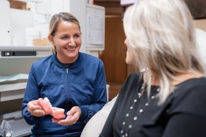 Hygienist showing patient a dental model while discussing cleaning frequency.